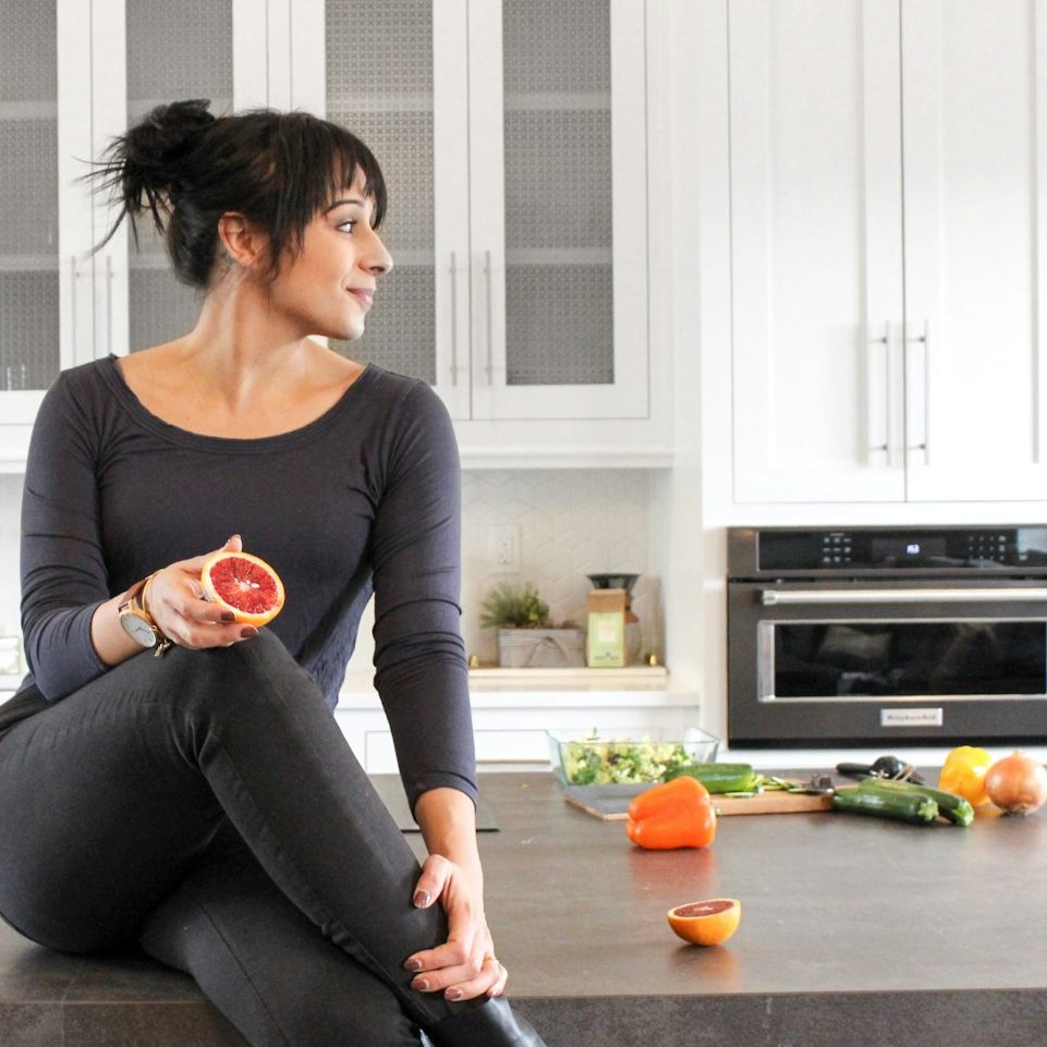 Eine Frau in sportlicher Kleidung sitzt in der Küche mit Gemüse und Obst