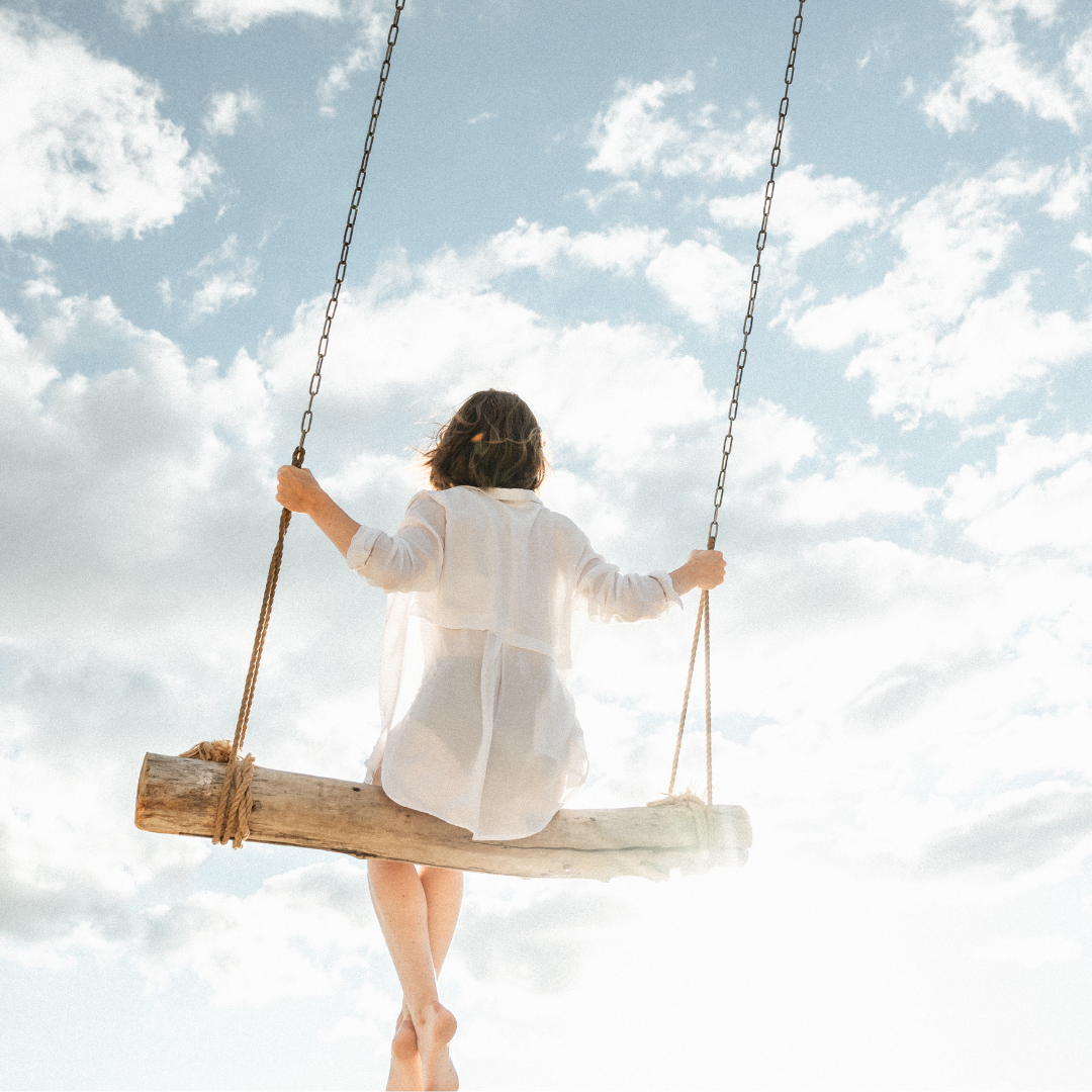 Frau schaukelt gelassen und entspannt unter blauem-weißem Wolkenhimmel