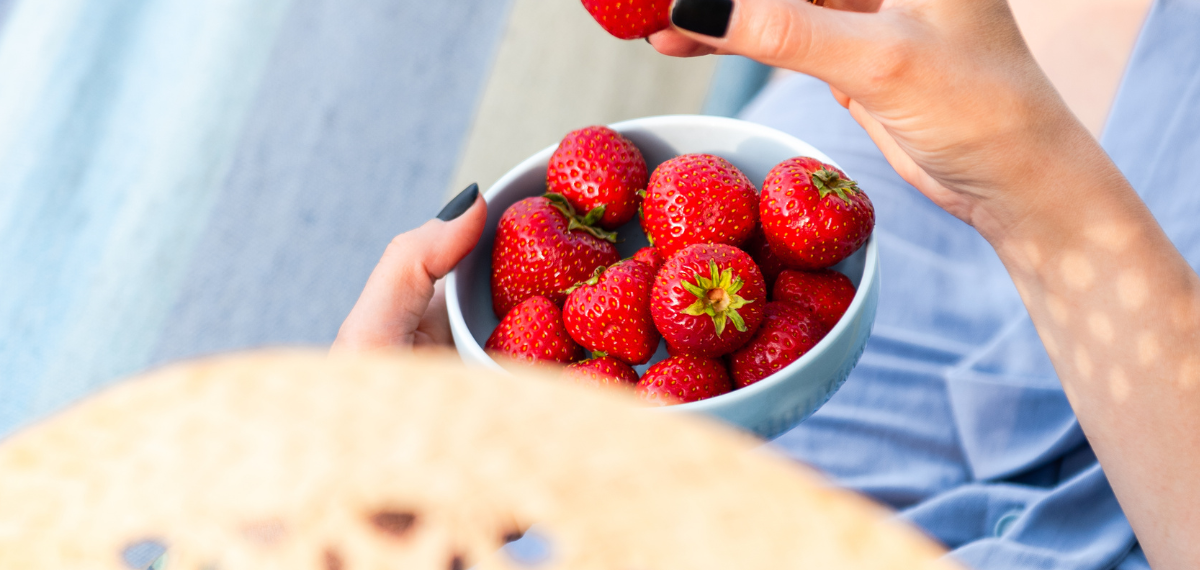 Frau nascht in der Sonne eine Schale Erdbeeren