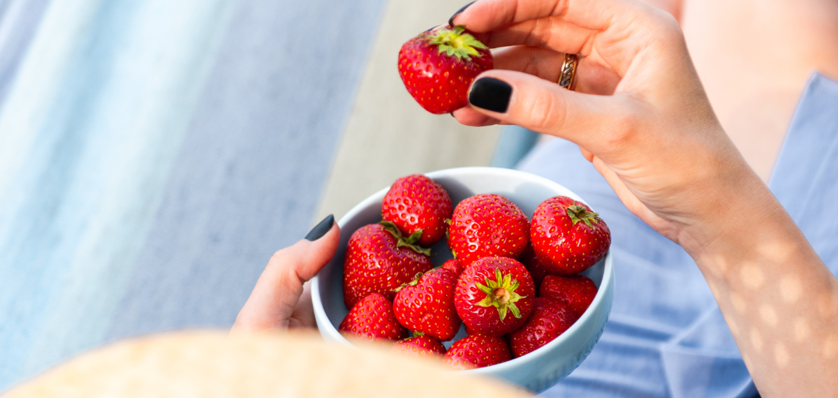 Frau nascht in der Sonne eine Schale Erdbeeren