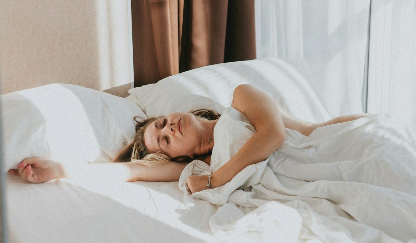 Frau schläft in weißer Bettwäsche entspannt